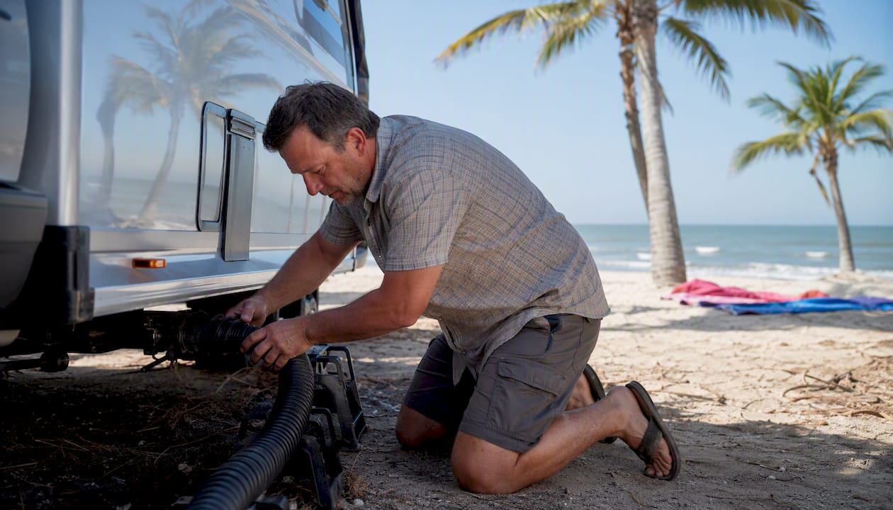 Man adjusting black tank sewer hose outdoors