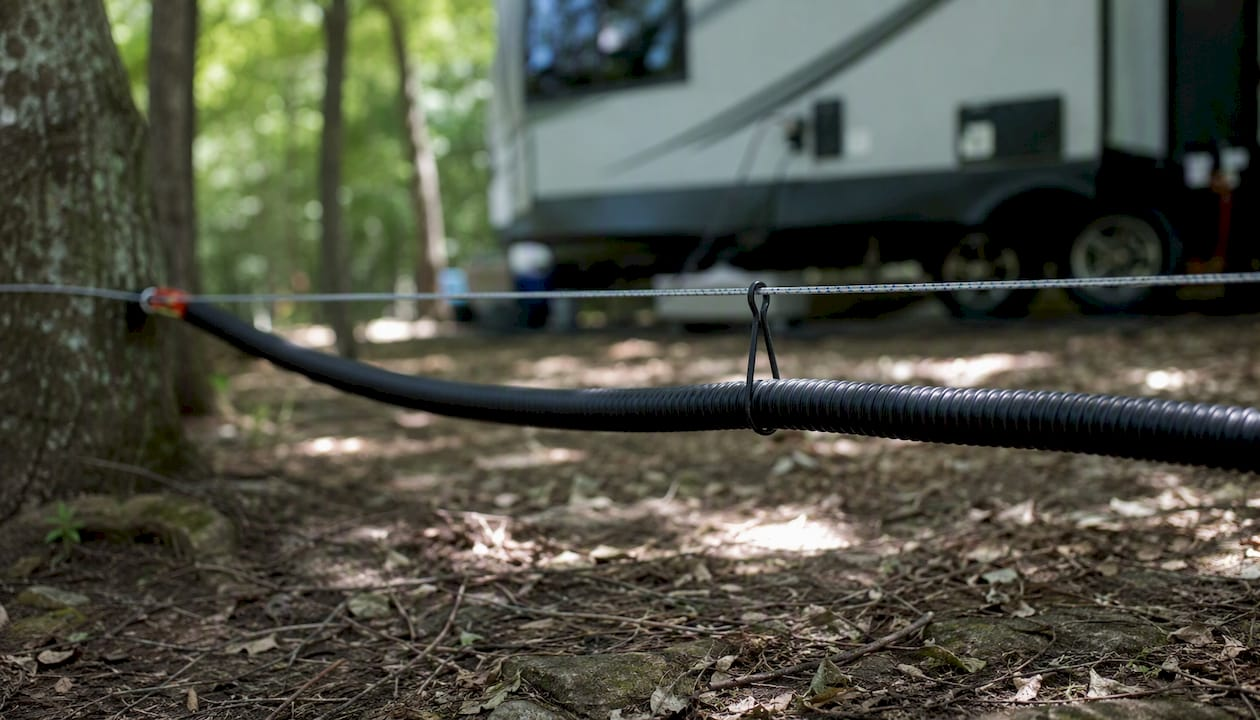 Tensioned sewer hose supported above gravel ground